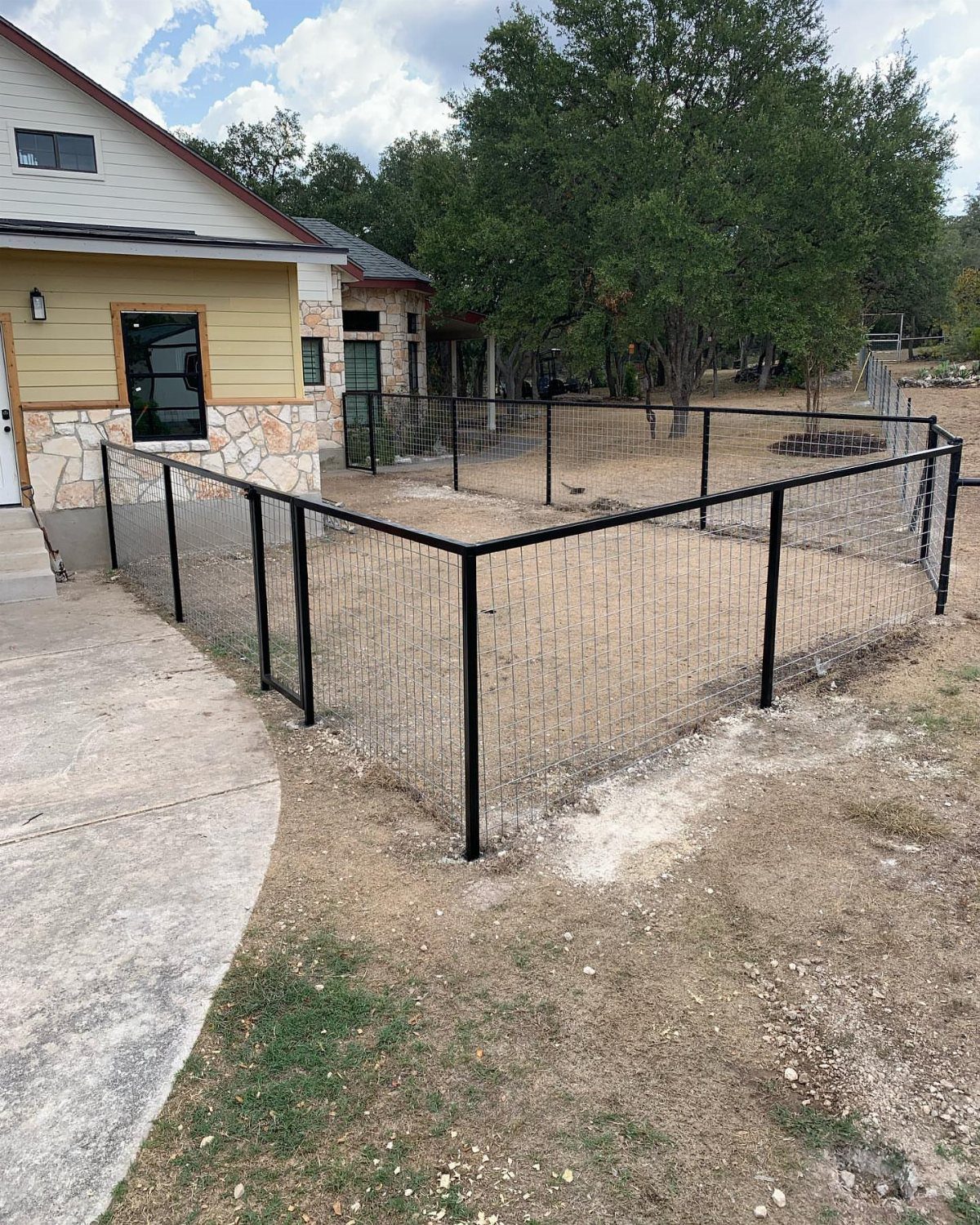 Black wire mesh dog fence enclosing a dirt yard area beside a house.