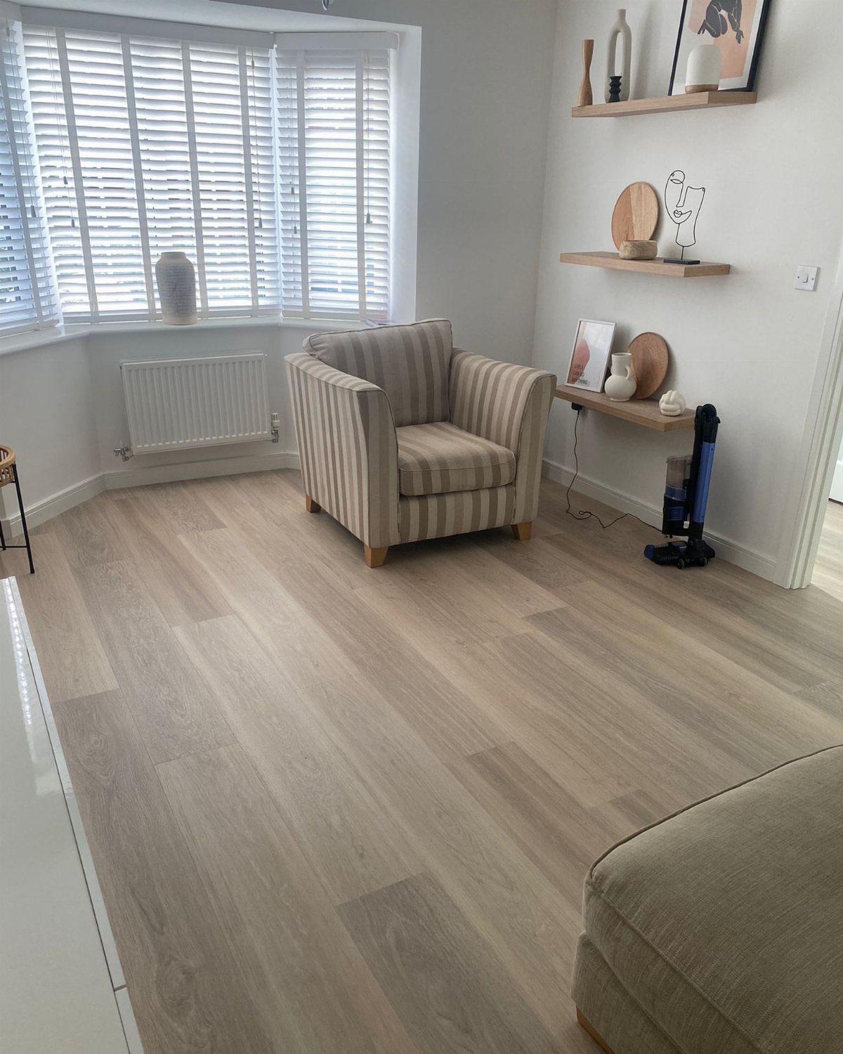 Light neutral oak effect flooring in a bright living room with a striped armchair.