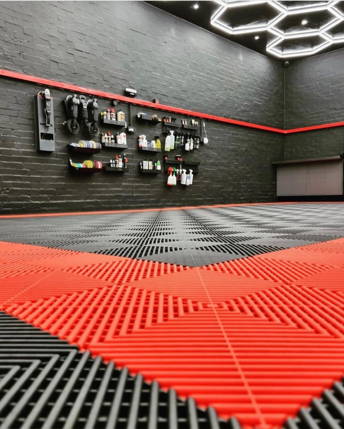 Red and black interlocking plastic tiles covering a garage floor in a geometric pattern.