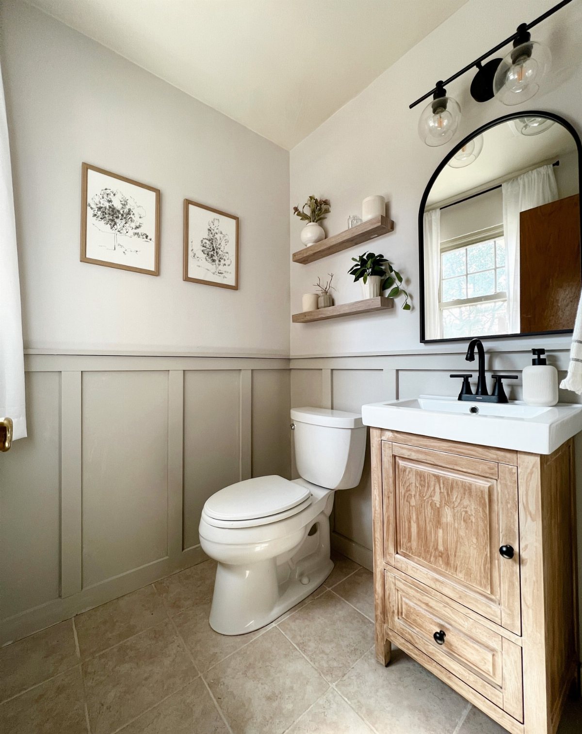 Small bathroom with a white toilet, wooden vanity, arched mirror, and grey wainscoting on the walls.