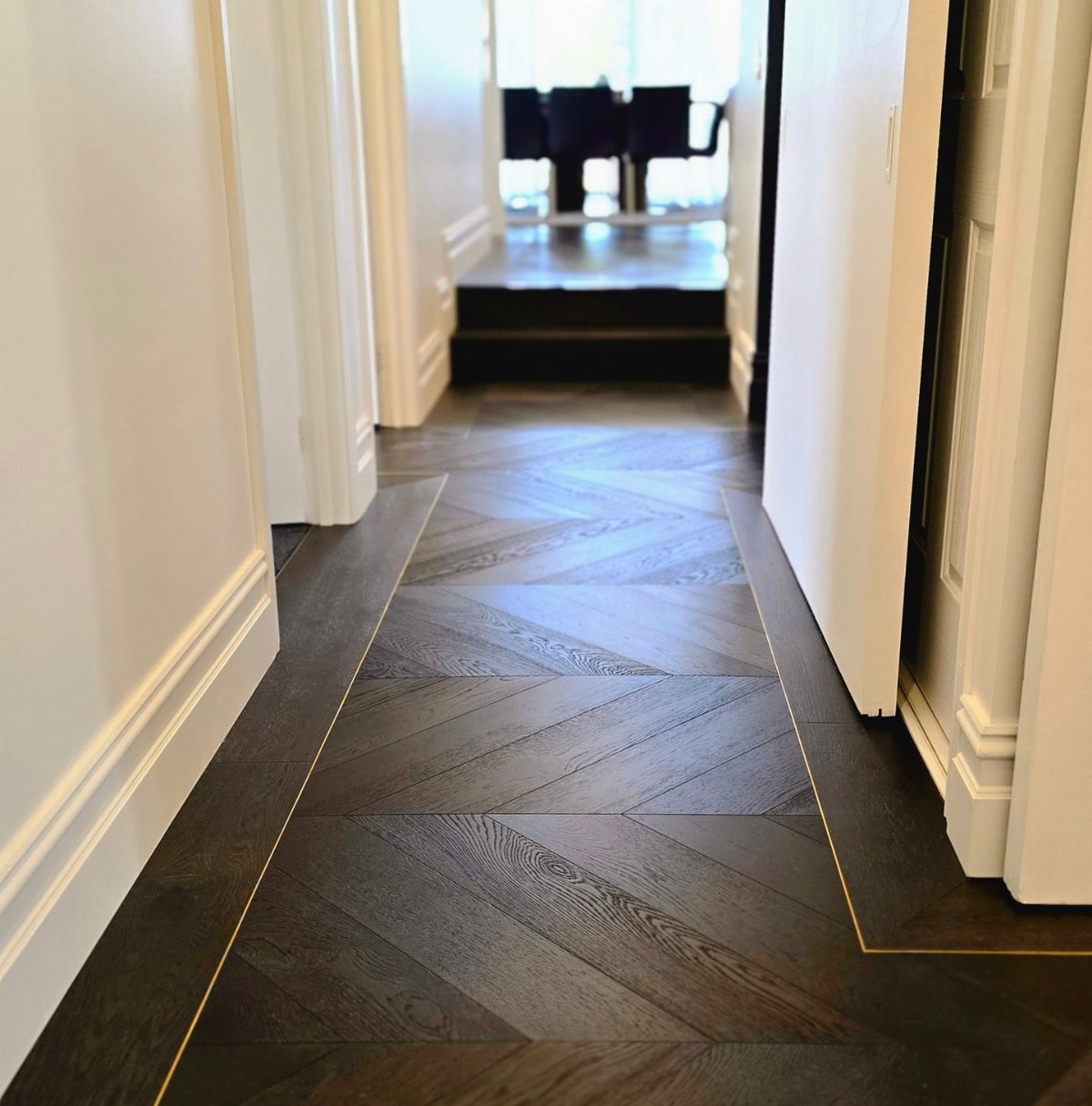 Dark wood herringbone flooring with gold inlay borders running through a white hallway.