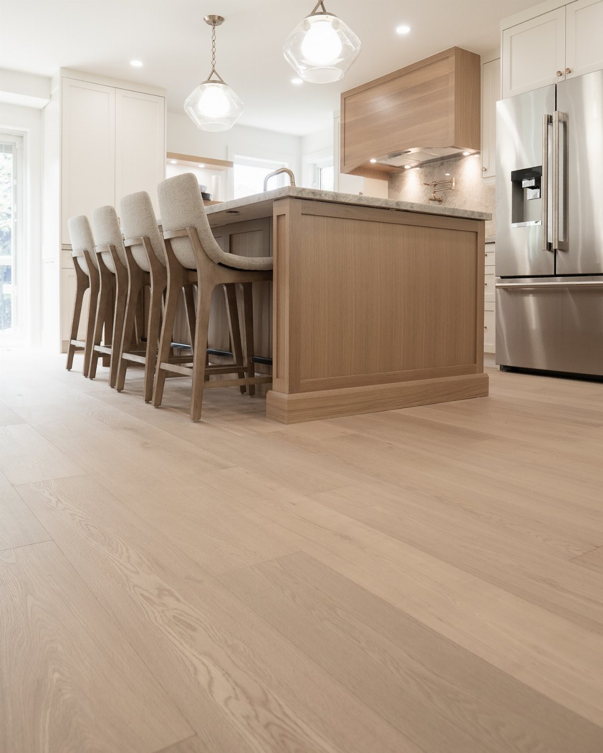 Light oak wood flooring stretching across a bright, modern kitchen with an island and stools.