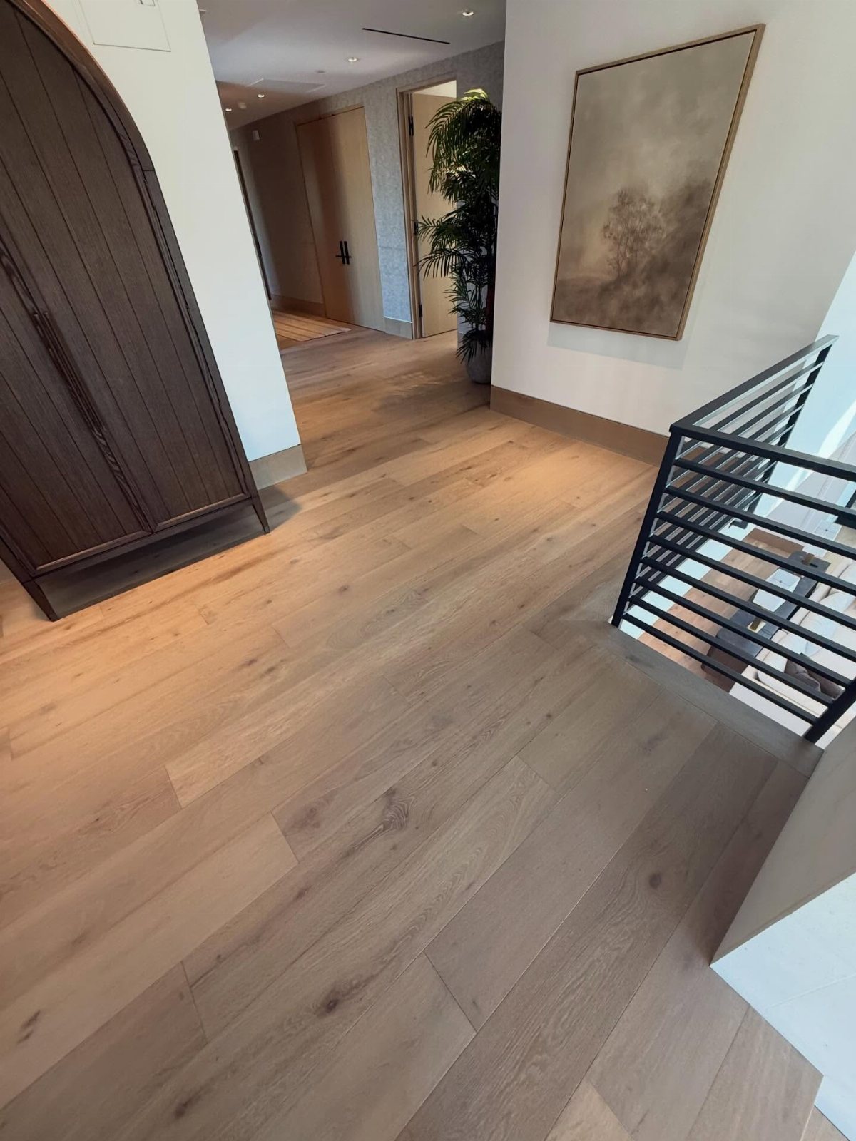 Light wood-look flooring planks running through a modern hallway with white walls and dark furniture.