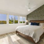 Light wood-look flooring in a bright bedroom with a large bed and coastal view windows.