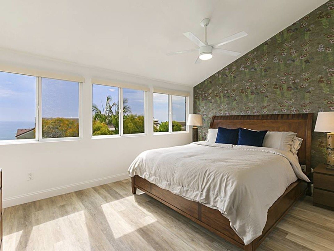 Light wood-look flooring in a bright bedroom with a large bed and coastal view windows.