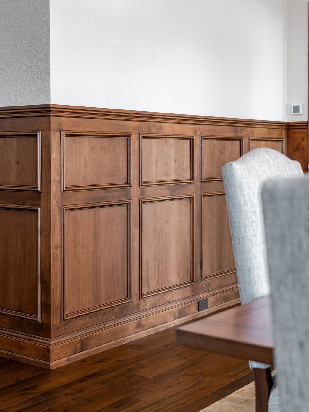 Dark wood wainscoting with raised rectangular panels installed on a white wall above dark wood flooring.
