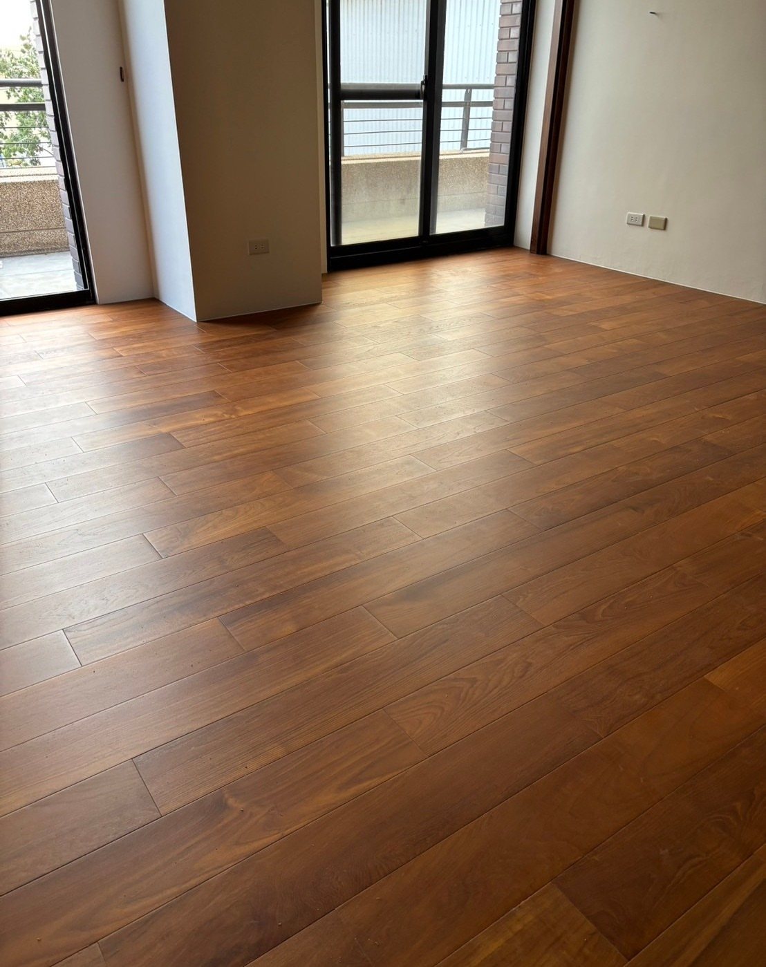 Polished medium-toned wooden floor planks in a bright, empty room with large glass doors.