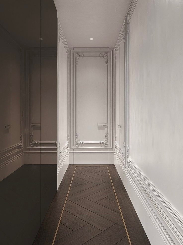 Dark brown chevron wooden flooring with light borders in a white paneled hallway.