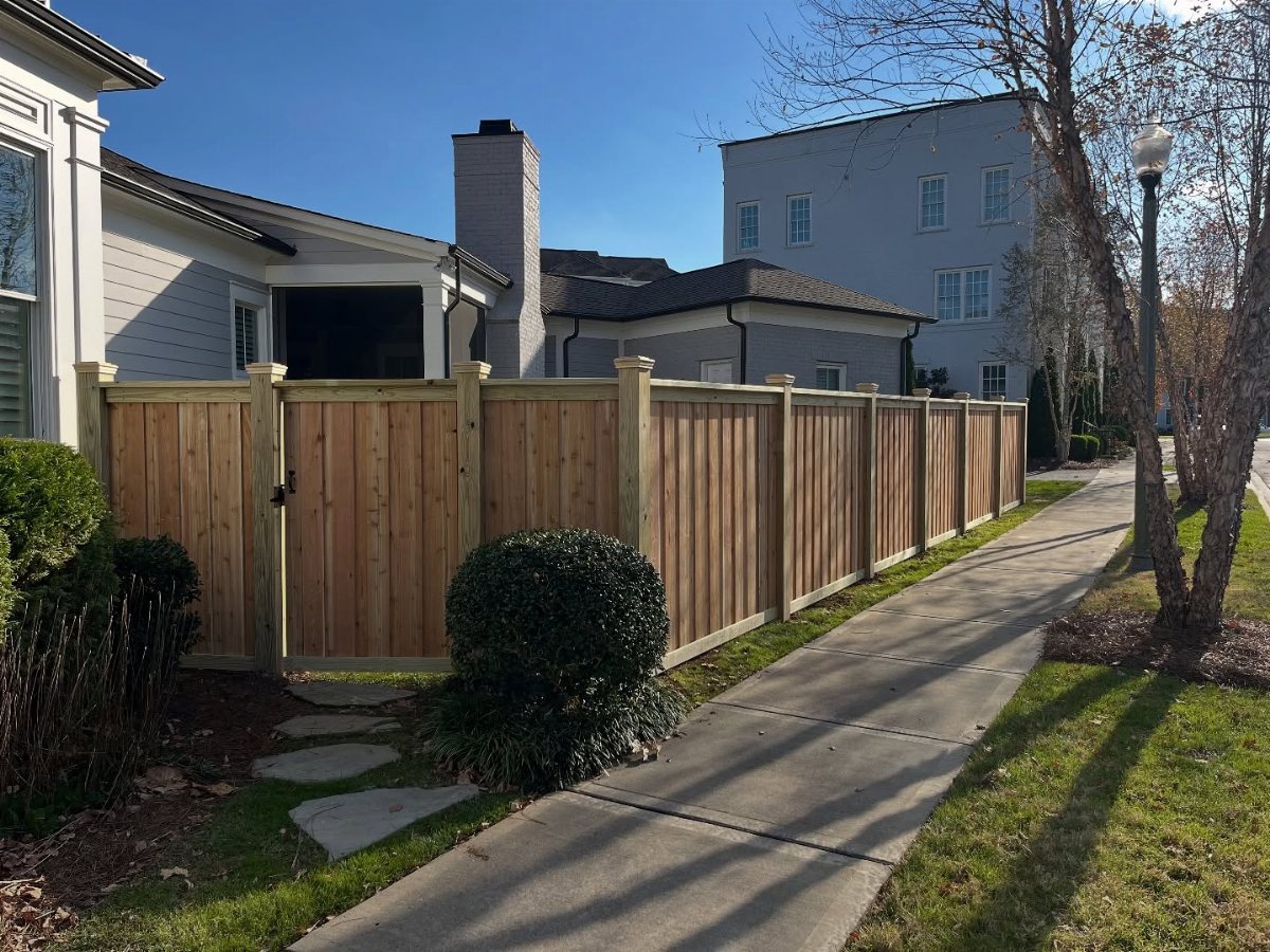 A long wooden privacy fence installed along a concrete sidewalk next to a residential house.